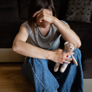 Femme assise sur le sol, tenant un ours en peluche, symbolisant la douleur et le chagrin d'une perte périnatale.