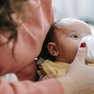 Bébé buvant son biberon dans les bras de sa maman.