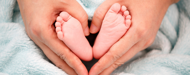 Pieds de bébé entourés de mains formant un cœur, symbolisant la douceur et les bienfaits de la réflexologie plantaire.