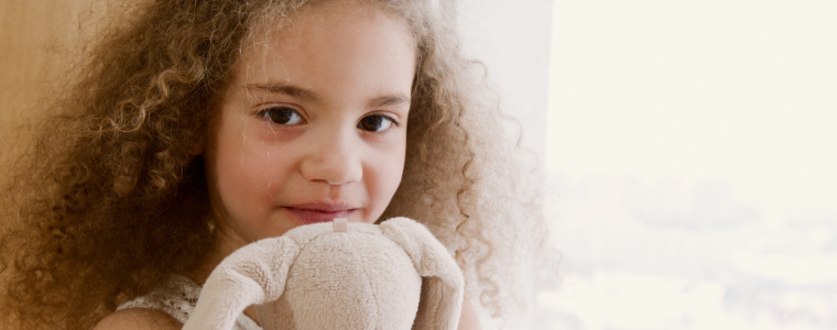 une petite fille souriante câlinant son doudou près d'une fenêtre