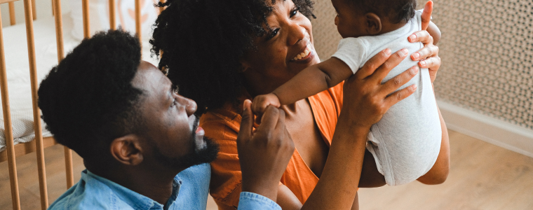 Parents souriants tenant leur bébé dans une chambre, illustration des tendances parentalité 2025.