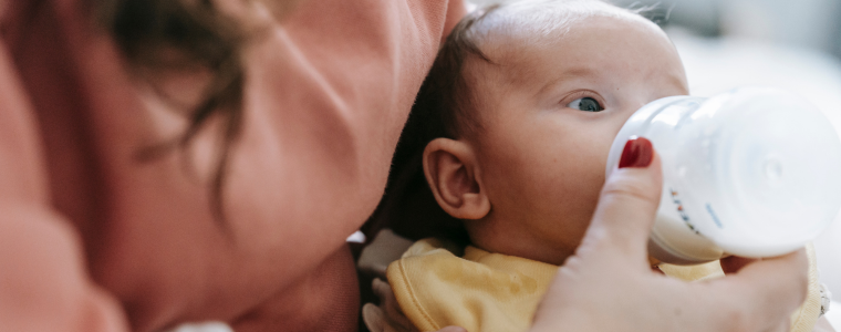 Bébé buvant son biberon dans les bras de sa maman.