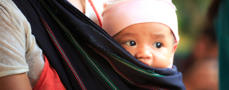 Un bébé confortablement installé dans une écharpe de portage noire avec des motifs colorés, porté par un parent.