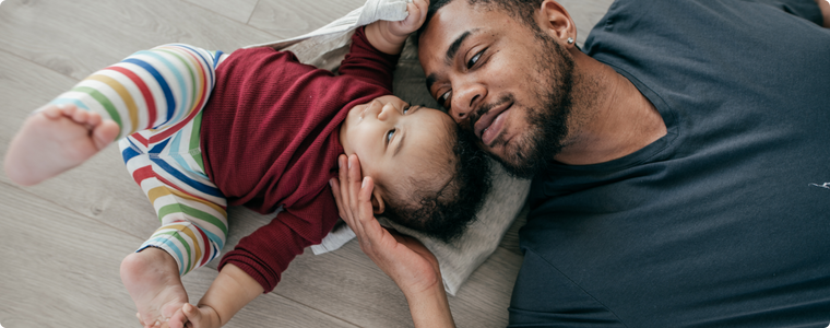 poussée de croissance bébé : papa apaise son enfant allongé au sol, échange de regards rassurant