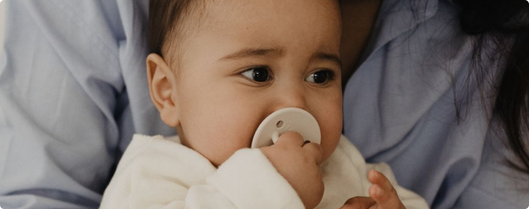 Bébé utilisant une sucette physiologique blanche, confortablement installé dans les bras de sa maman