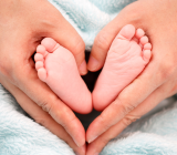 Pieds de bébé entourés de mains formant un cœur, symbolisant la douceur et les bienfaits de la réflexologie plantaire.