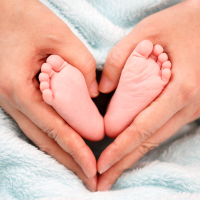 Pieds de bébé entourés de mains formant un cœur, symbolisant la douceur et les bienfaits de la réflexologie plantaire.