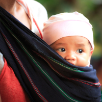 Un bébé confortablement installé dans une écharpe de portage noire avec des motifs colorés, porté par un parent.