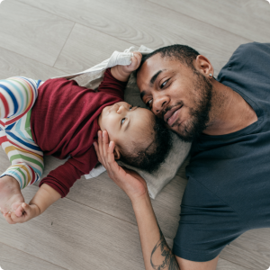 poussée de croissance bébé : papa apaise son enfant allongé au sol, échange de regards rassurant